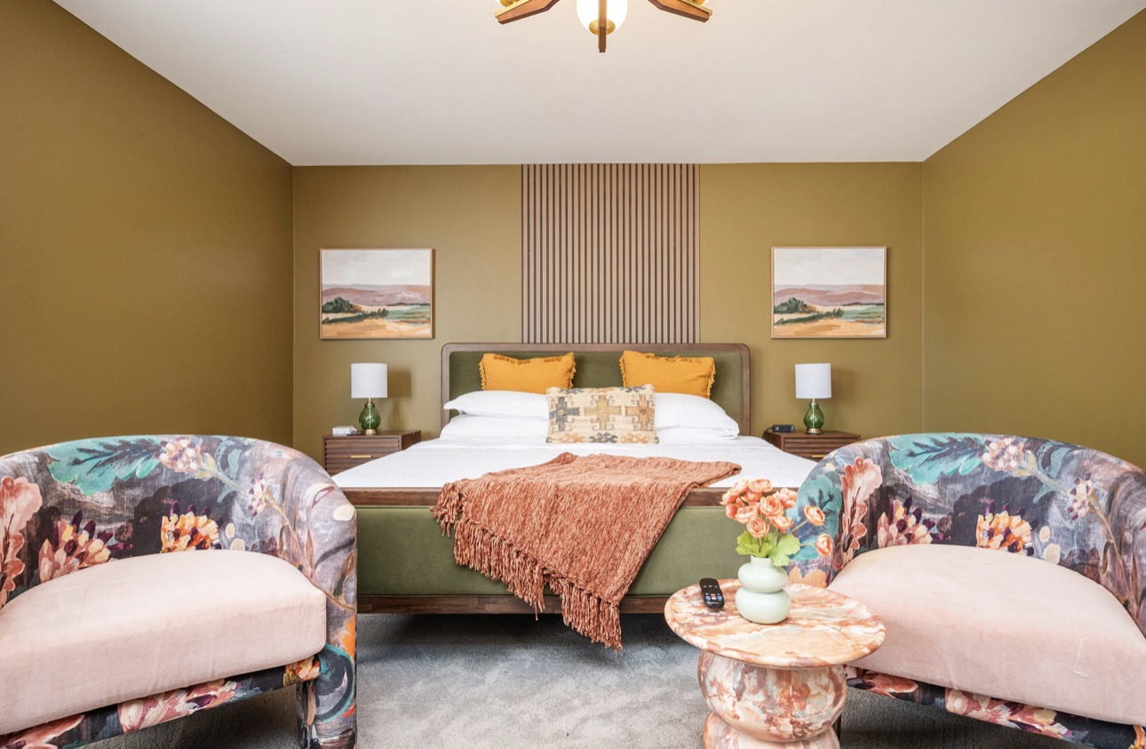 Bedroom with olive walls, layered bedding, and patterned accent chairs