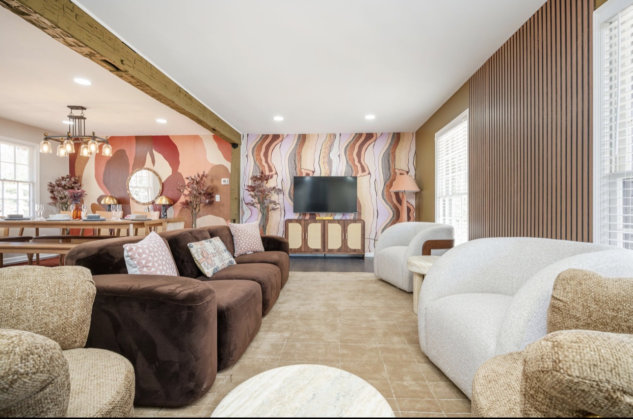 Living room with wavy wallpaper, wood-slat accent wall, bouclé barrel chairs, and a round mirror opening to a dining area